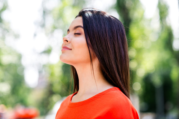 照片漂亮的青少年好心情的女孩闭上眼睛享受阳光明媚的天气穿着红色的衣服走在城市城市公园外图片下载