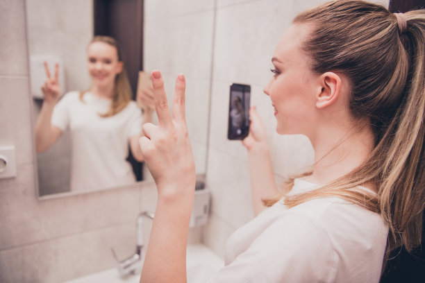 照片积极的好心情女孩睡衣说话镜自拍现代设备显示v字室内房子公寓洗手间图片下载