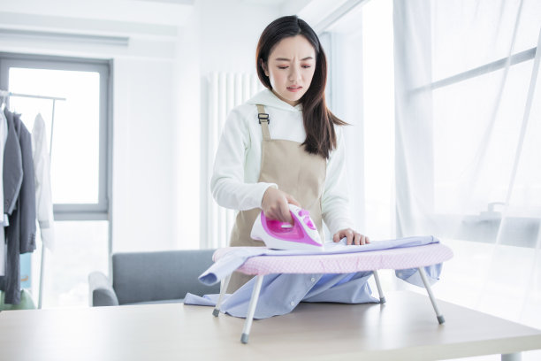 快乐的年轻美丽的女人熨衣服。做家务图片下载