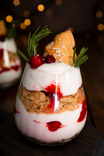 一杯圣诞甜点，姜饼饼干，鲜奶油和蔓越莓在深色木制背景-照片与金色散景图片下载