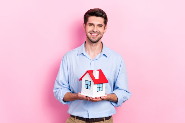照片正面成功的男子持有微型房子展示广告房地产服务孤立的粉红色背景图片下载