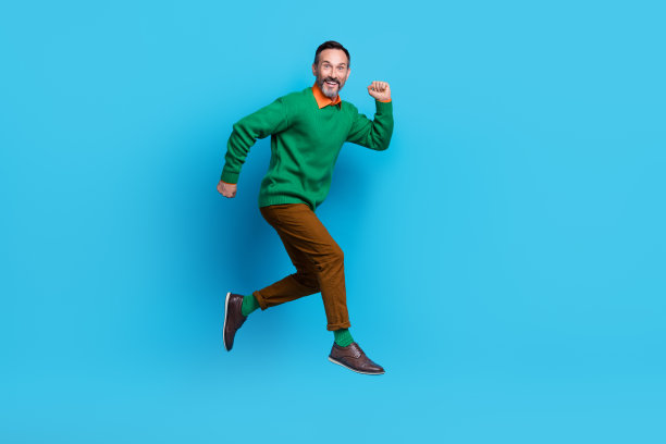成熟的漂亮先生的全长照片精力充沛的奔跑跳跃匆忙穿着时尚的绿色服装孤立的蓝色背景图片下载