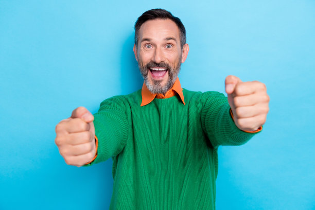 照片肖像中成熟迷人的男性兴奋地握着看不见的方向盘，穿着时髦的绿色，在蓝色的背景上显得孤立图片下载