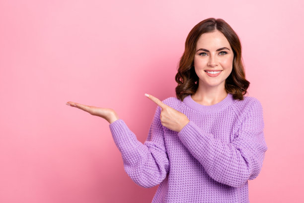 快乐愉快的女人的照片波浪发型编织毛衣手掌示范对象指向空白空间孤立在粉红色的背景图片下载