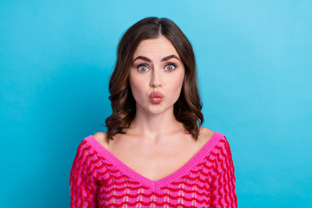 照片有趣的年轻兴奋噘嘴迷人的女孩吻丰满你穿时髦的粉红色针织上衣的衣服孤立在蓝色的背景图片下载