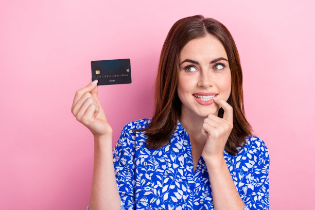 有吸引力的创意女孩的照片，手指触摸嘴唇，手握借记卡，看起来空白的空间孤立在粉红色的背景图片下载