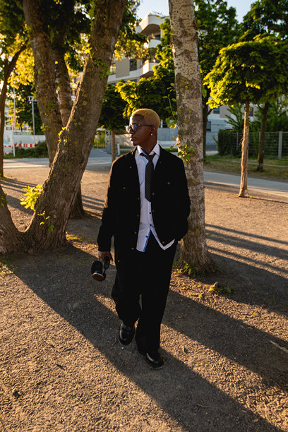 外面一个留着黄色发型的黑人男性肖像，他戴着无线耳机。人穿深色西装和白色衬衫。与帅哥的生活方式摄影。图片下载