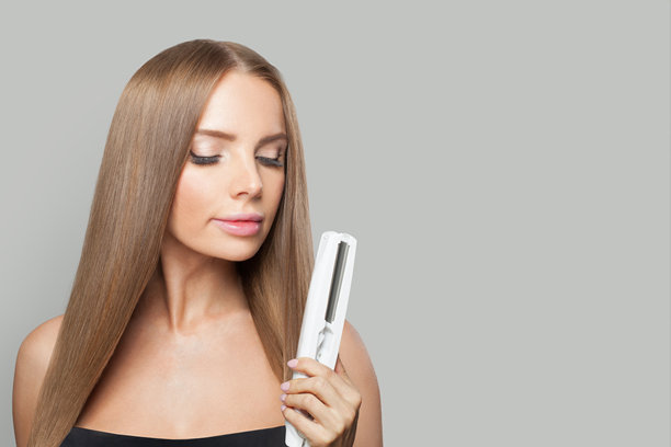 深色头发，直发的女人拿着白色背景的直发棒。女性美容、美发、护发、化妆及造型理念图片下载