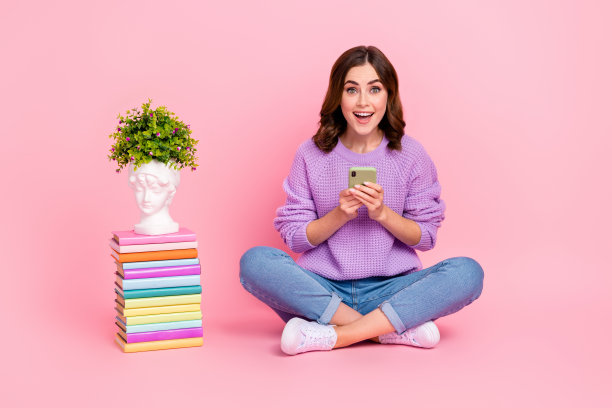 印象深刻的时髦女孩穿着紫色套头衫购买现代设备书堆栈孤立的粉红色背景的完整的照片图片下载