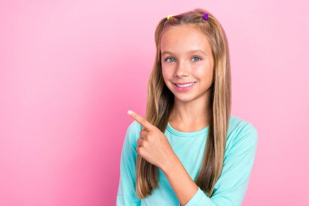 小可爱的小女生的特写照片穿青色的衬衫牙齿微笑手指点空空间好消息信息孤立在粉红色的背景图片下载