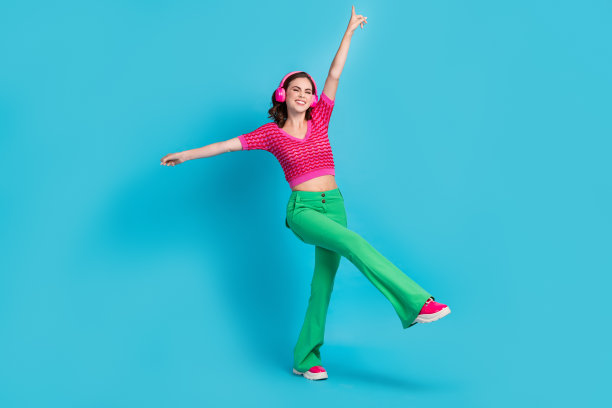 满意的甜美漂亮女孩的全身照片，卷发，穿着粉红色的上衣，跳舞举起手，孤立在蓝色的背景上图片下载