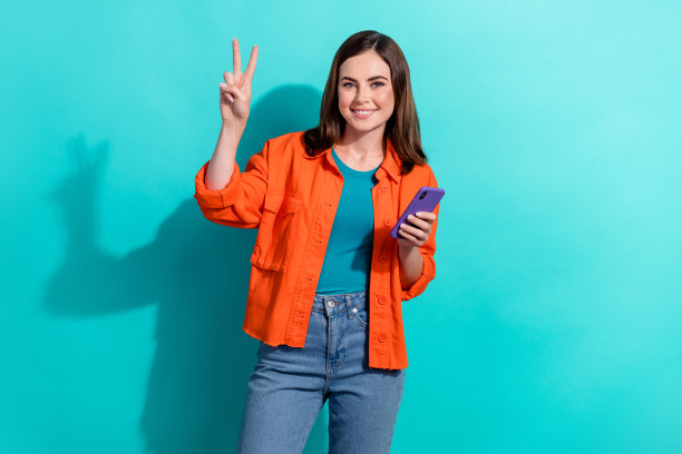 积极漂亮的博主用户在海蓝宝石背景上展示v-sign提升质量的设备小工具的照片图片下载