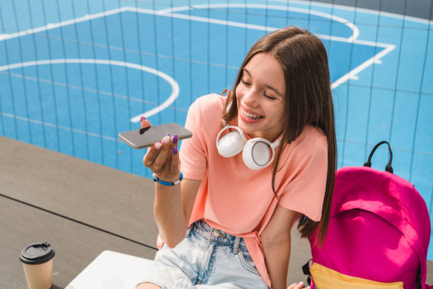 积极的高中女生穿着便服戴着耳机用电话录音图片下载