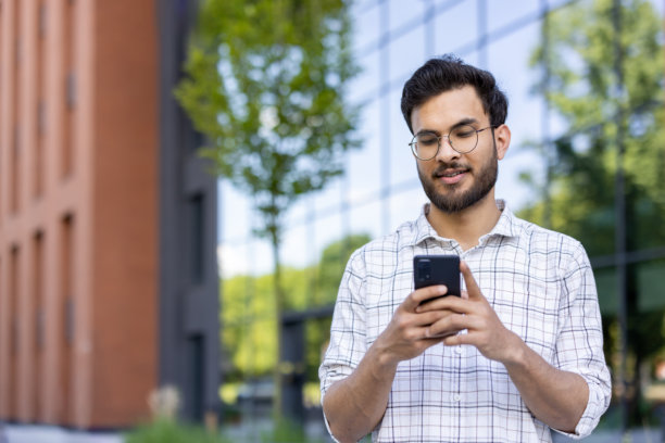 印度年轻男子站在办公中心外，专注于使用智能手机的特写照片图片下载