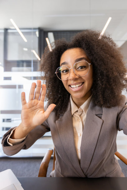 一个年轻的非裔美国女商人在办公室的垂直照片，拿着相机在视频通话。微笑和挥手图片下载