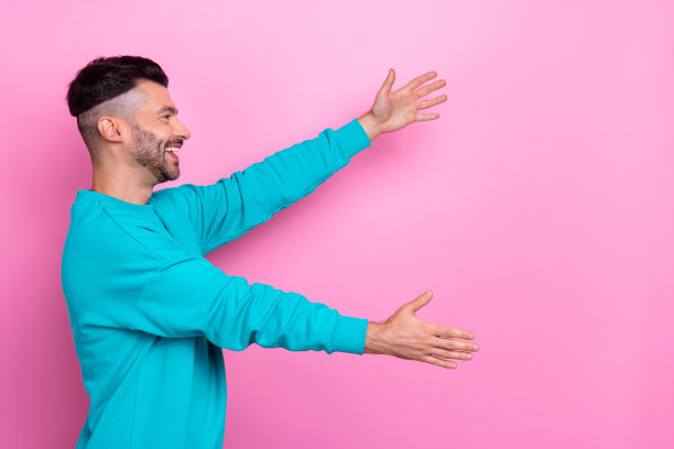 侧面侧面照片的年轻友好的学生，男子气概的家伙，深色头发，穿蓝色运动衫，想拥抱空白空间孤立在柔和的粉红色背景图片下载