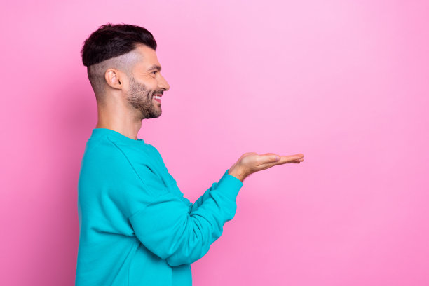 年轻乐观的男子学生手牵手的个人资料照片展示了新产品的最佳质量，看起来空白的空间孤立在粉红色的背景图片下载