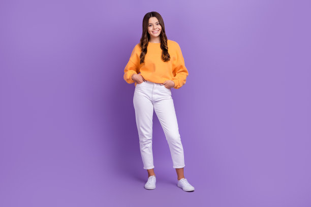 甜美可爱的女孩全身照片穿着橙色运动衫微笑着走孤立的紫色背景图片下载