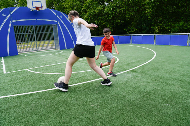 母亲教儿子在阳光下一起在绿色的草地上踢球图片下载