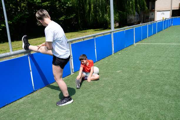 比赛前，儿子和母亲在足球场上伸着懒腰。图片下载