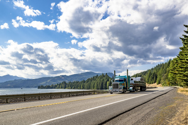 绿色经典大钻机半卡车拖拉机与高排气管运输木材货物在平板半挂车沿哥伦比亚河在哥伦比亚峡谷地区的高速公路上运行图片下载