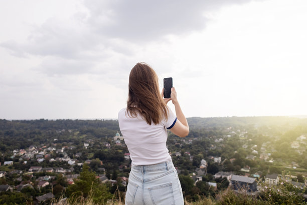一位年轻女子用手机拍下了山顶上美丽的城市景色。智能手机上的照片和视频。旅游博主和影响者图片下载