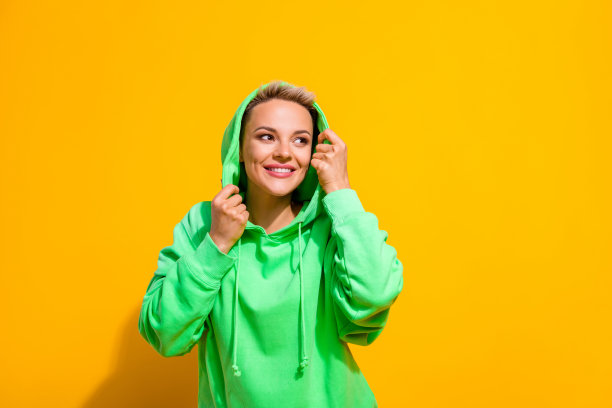 照片迷人的微笑开朗的女士短金发戴时尚的绿色兜帽看起来空白空间品牌广告孤立在黄色的背景图片下载