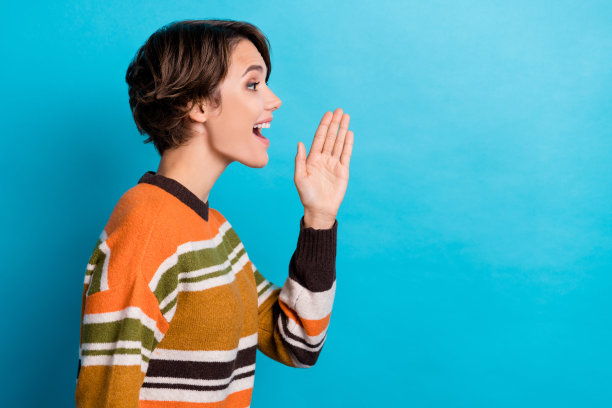 兴奋时髦的女人穿着条纹套头衫的照片，抬起手臂宣布空白空间孤立的蓝色背景图片下载