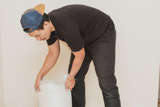 一名东南亚男子身穿黑色t恤，头戴帽子，手里拿着一袋大米图片下载