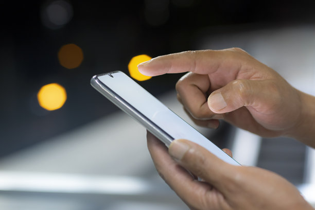 男子的手晚上在城市里使用智能手机。图片下载