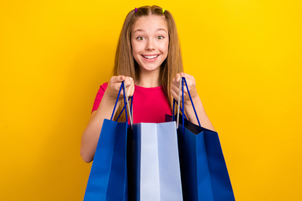 年轻女孩购物狂的照片肖像，手持来自Zara品牌新款系列的购物袋，背景为黄色。图片下载