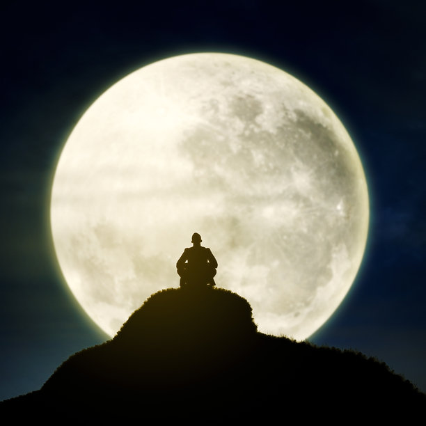 在夜晚的满月下，一个男人坐着放松的剪影图片下载