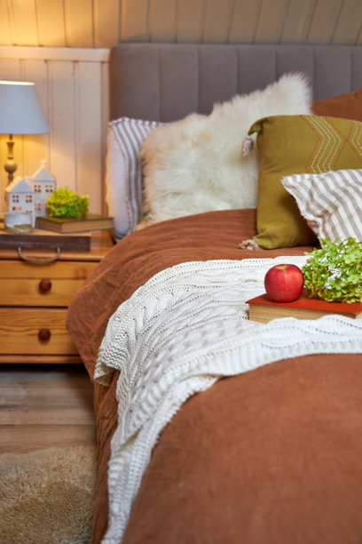 Wooden nightstand next to the bed decorated with textiles and pillows in modern style图片下载