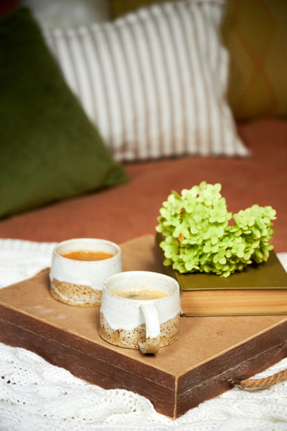 A serving tray with coffee cups and flowers stands on the bed in the bedroom图片下载