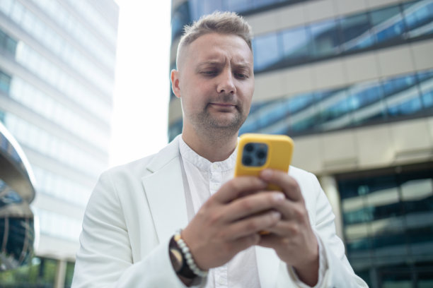 专注且愤怒的年轻企业员工投资者在商业中心附近走动并使用手机。图片下载