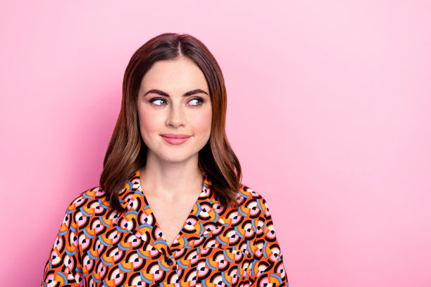 漂亮年轻女孩的照片肖像，目光充满兴趣，穿着时尚印花服装，站在粉色背景前，适合购物促销。图片下载