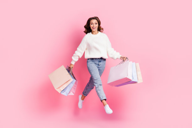 穿着白色毛衣的酷炫兴奋女士在粉色背景上跳跃行走，手中拿着购物袋的全身照片图片下载