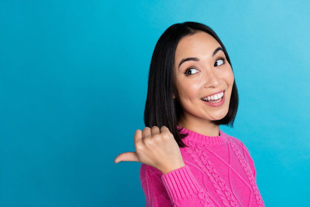 微笑的漂亮泰国女士的个人资料照片，手指指向蓝色背景上的空白空间。图片下载