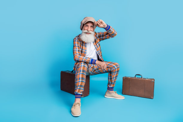 快乐的祖父坐着，手触摸头饰，背景为蓝色的全身照片图片下载