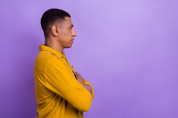 侧面照片，阳光帅气的男士穿着黄色衬衫，双臂交叉，目光投向空旷的空间，背景为紫色。图片下载