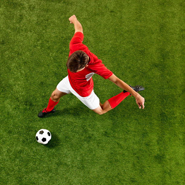 年轻的足球运动员身穿红白色装备，精准训练中运球，保持对球的控制，场馆上空视角。图片下载