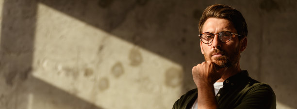 戴眼镜的设计师在混凝土墙旁看向镜头的肖像，网页横幅图片下载