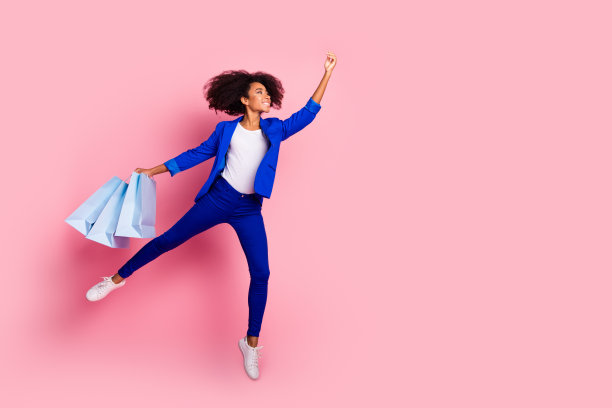 穿着蓝色夹克的可爱女孩手持购物袋，目光投向空旷的空间，背景为粉色。图片下载