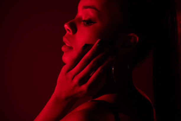 非洲女孩的侧面特写照片，轻柔地触摸脸庞，背景为渐变霓虹红色。图片下载