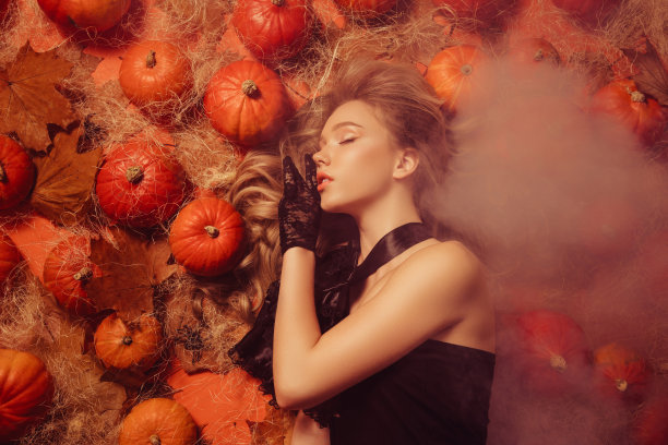 俯视图照片：迷人的女士躺在万圣节的薄雾中，身旁有南瓜，沉睡中梦见可怕的夜晚。图片下载