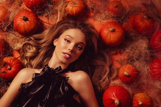 俯视照片中，一位身穿黑色贵族服装的迷人女士躺在万圣节装饰的南瓜旁，散发出诱惑的魅力。图片下载