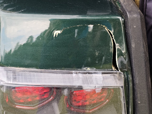 绿色汽车的油漆有明显的损伤，尾灯附近有裂缝。图片下载