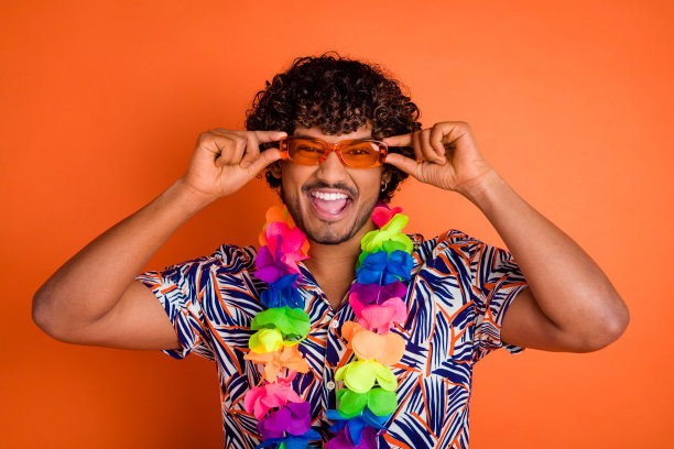 漂亮的年轻人的照片肖像触摸太阳镜享受夏天穿时髦的彩色服装孤立的橙色背景图片下载