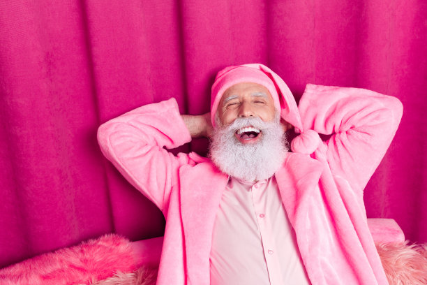 照片中的圣诞老人戴着浴袍帽睡觉，旁边是粉红色的窗帘背景图片下载