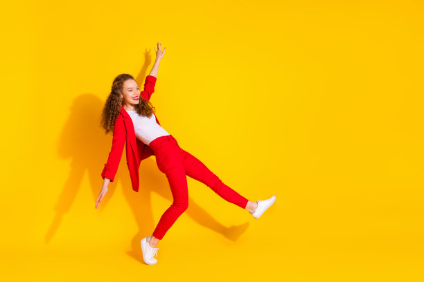 穿着红色西装的漂亮年轻女性在黄色背景下的空旷空间中轻松舞蹈的全身照片图片下载